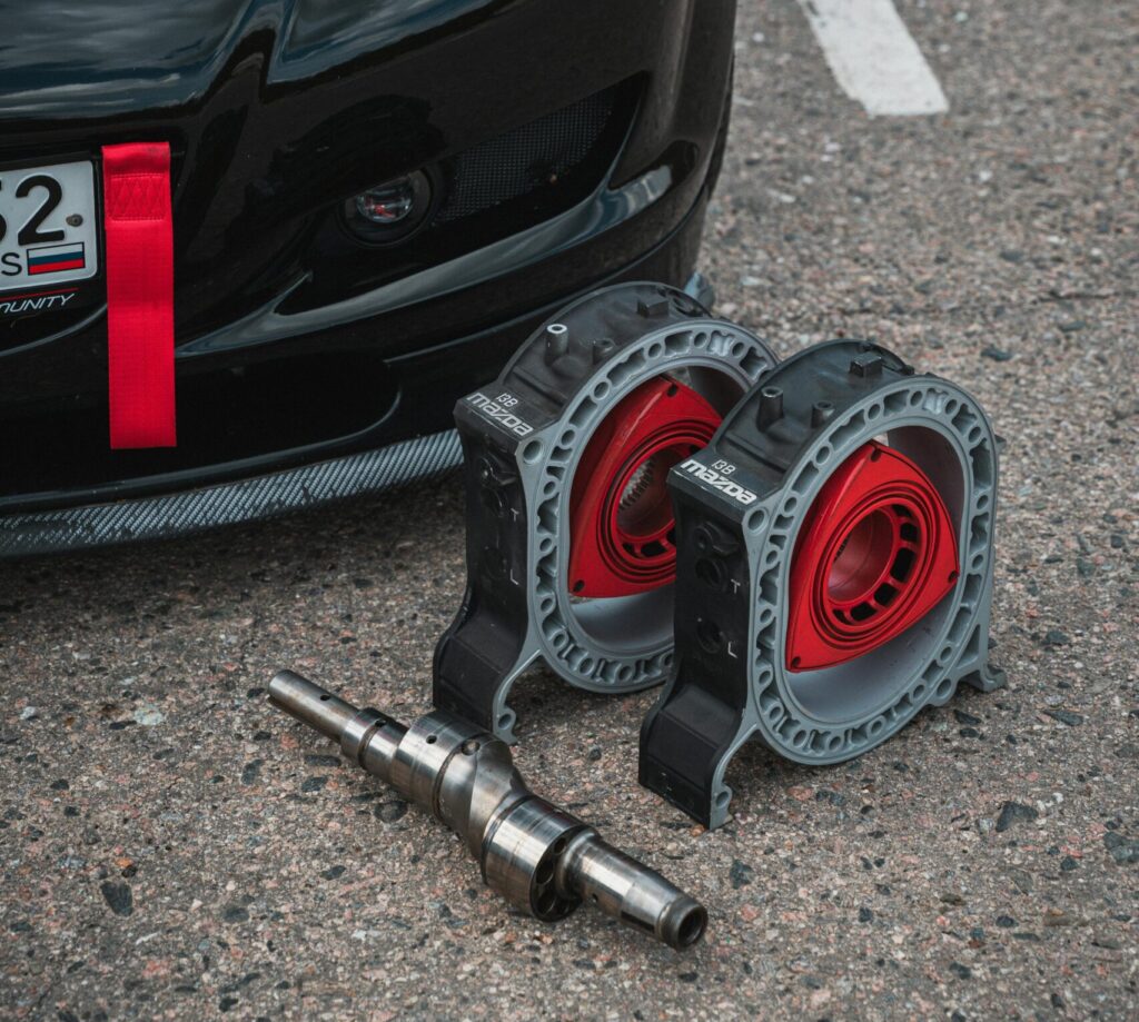 Detailed view of car engine parts on asphalt near a black sports car, showcasing automotive maintenance.