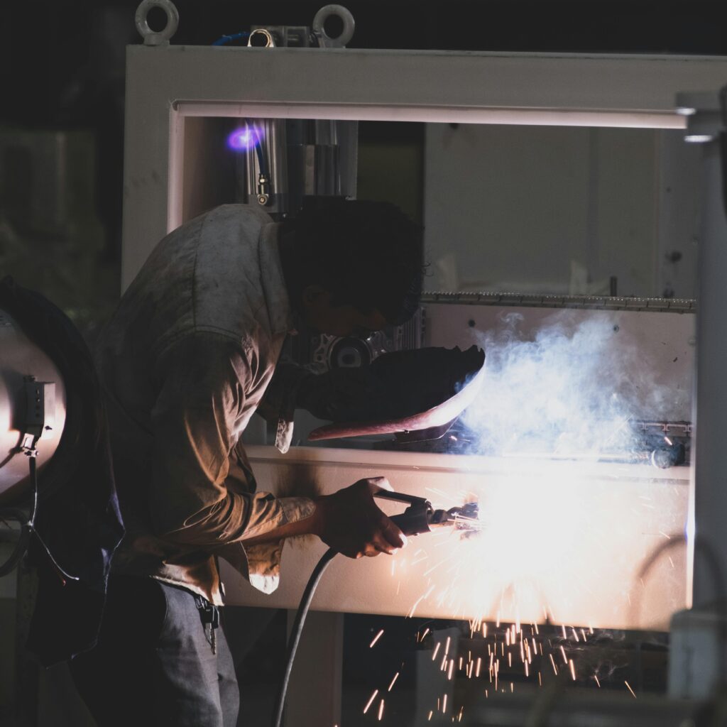 Welder using protective gear, creating sparks while welding indoors in Mumbai.