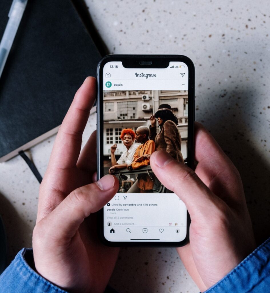 Close-up of hands holding a smartphone browsing Instagram with a notebook and pen nearby.